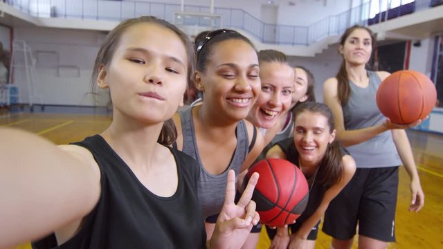 POV of young multiethnic basketball girls smiling and posing for camera while taking a selfie together on court