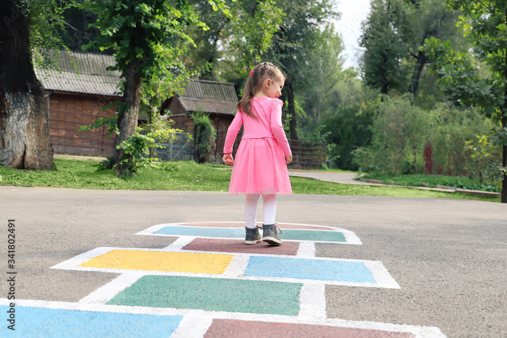 Wall mural Young cute girl playing hopscotch on backyard