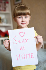 Stay at home - an inscription on a paper sheet in the hands of a girl child. During the COVID-19 Coronavirus pandemic