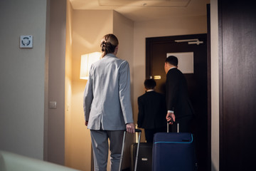 A family in formal wear leaving a hotel room with their suitcases