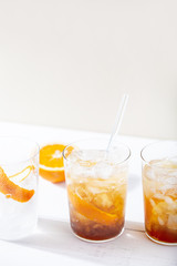 Cold brew coffee mocktail with orange peel and glass straw.Glass with citrus espresso tonic with ice on white background.Refreshing summer non-alcoholic drink concept.Vertical orientation,copy space