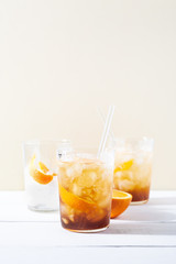Cold brew coffee mocktail with orange peel and glass straw.Glass with citrus espresso tonic with ice on white background.Refreshing summer non-alcoholic drink concept.Vertical orientation,copy space