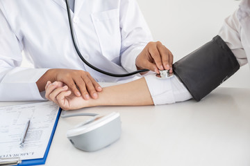 Doctor evaluates the patient with a stethoscope, blood pressure monitor and records the results, health medical checkup concept