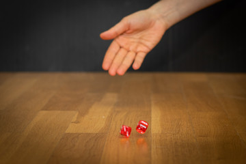 main jetant deux dés rouges sur le plancher de parquet avec le fond noir