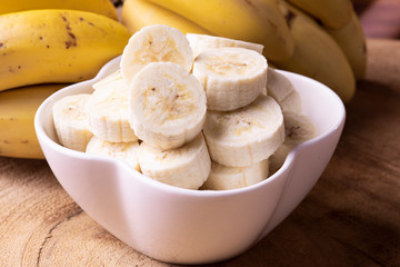 
Bananas cut in a bowl with some bananas in the background