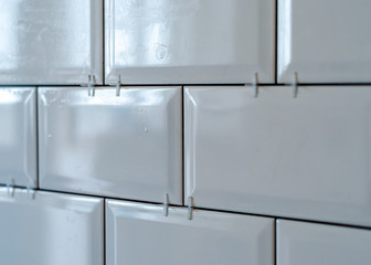 Ceramic tile laying. Placing white tile spacers. Installed new white rectangular ceramic tile inside apartment, bathroom or kitchen back splash during home renovation.