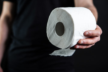 Close-up detail on a man's hand as he holds a white roll of toilet paper on the black background. The topic is about Corona virus - COVID 19