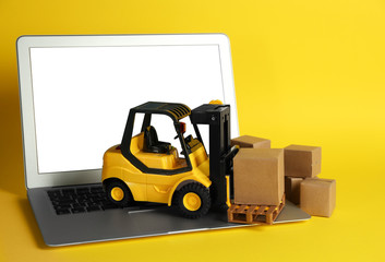 Laptop, forklift model and carton boxes on yellow background. Courier service © New Africa