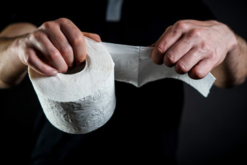 Detail close-up of man's hands tearing white toilet paper on a black background.