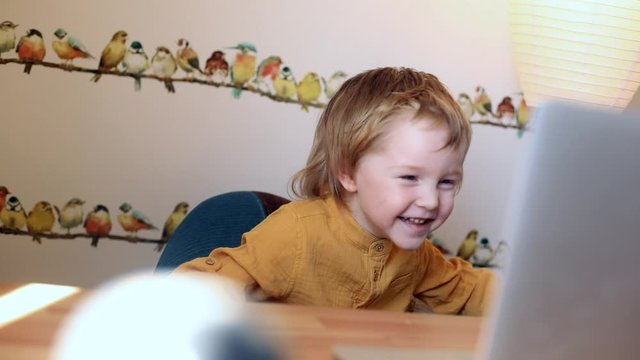Happy laughing little boy using laptop for video call, looking cartoons and learning online with friends and family. Sunny background. Children entertainment. Technology. Internet. Education 