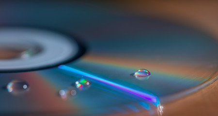 A drop of water on a multi-colored CD - disk. Blurred background, wallpaper. Flat lay, copy space. Abstract. Creative. Macro.