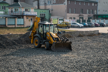 UKRAINE, LUTSK - April 10, 2020: Yellow wheel loader Excavator machine working at construction site with gravel. Preparing of the fundament for a asphalting. Road construction site.