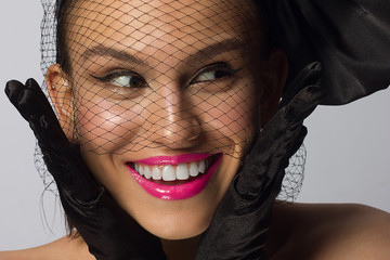 Fashionable half beauty of a woman with a knot and veil, black eyeliner and pink lipstick. Clean and radiant skin, natural lip gloss, thick eyebrows and long eyelashes. Cosmetology and makeup.