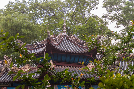 Fengdu, China - May 8, 2010: Ghost City, historic sanctuary. Closeup of Brown Chinese architectural roof structure under green foliage. Some blue, green and yellow painted decorations.