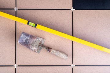 Laying gres tiles on warehouse spaces. Old spirit level and trowel for laying mortar.