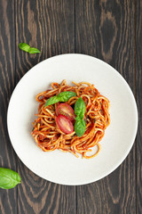 Tasty appetizing classic italian spaghetti pasta with tomato sauce, fresh cherry tomatoes and basil on ceramic plate. Wooden background, rustic style. Top view.