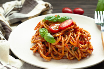 Tasty appetizing classic italian spaghetti pasta with tomato sauce, fresh cherry tomatoes and basil on ceramic plate. Wooden background, rustic style. 