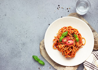 Vegetarian appetizing pasta served with tomato sauce, basil and fresh cherry tomatoes on ceramic plate. Light grey concrete background. Top view.
