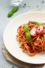 Vegetarian appetizing pasta served with tomato sauce, basil and fresh cherry tomatoes on ceramic plate. Light grey concrete background. Close up.