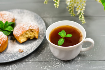 Composition with a cup of tea, cupcakes and white cherry flowers on a wooden background.
