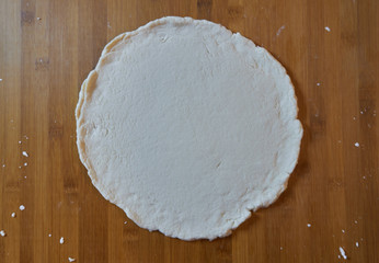 Fresh round homemade thin pizza dough crust on floured wooden board made with a gluten-free flour....