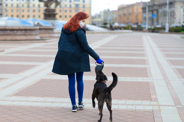 Young female using a face mask as a coronavirus spreading prevention walking with her dog. Global...