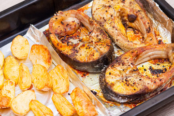 Baked steakes of white fish silver carp, potatoes, spices in a cooking tray or deco.