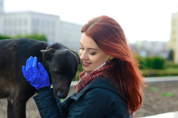 Young female using a face mask as a coronavirus spreading prevention walking with her dog. Global...