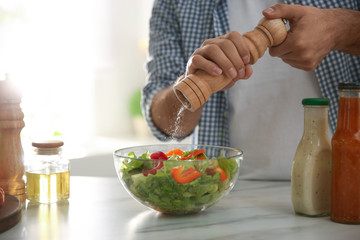 Man cooking salad at table in kitchen, closeup