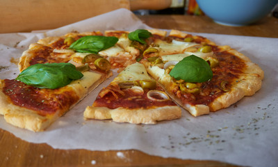 Fresh gluten-free homemade pizza with a thin dough crust olives basil and onions mozzarella cheese and tomato sauce, on a baking sheet paper
