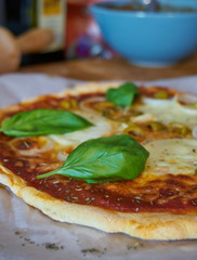 Fresh gluten-free homemade pizza with a thin dough crust olives basil and onions mozzarella cheese and tomato sauce, on a baking sheet paper