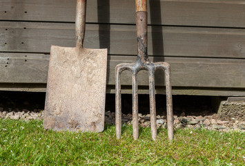 Garden spade and fork leaning against a wooden shed