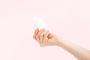 White cosmetic cotton pad in a woman hand on pink background. Make up remover pad, absorbent for micellar water, cotton sponge. Palm facing up.  © Snizhana