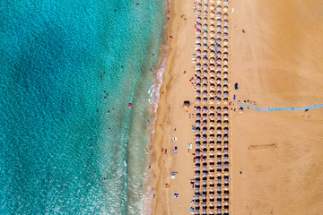 Aerial view of sandy beach with colorful umbrellas, swimming people in sea bay with transparent blue water at sunset in summer. Aerial top view on the beach, umbrellas, sand and sea waves.