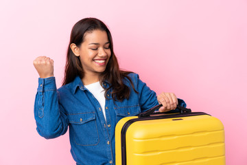 Traveler Colombian woman holding a suitcase over isolated pink background celebrating a victory