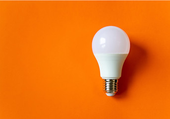 White energy saving light bulb on an orange background with copy space. LED white bulb, concept of...