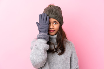 Young Colombian girl with winter hat over isolated pink wall covering a eye by hand