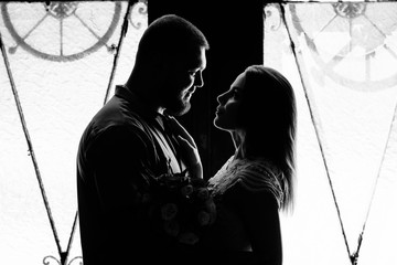 portrait of a romantic couple in a backlight from a window or door, silhouette of a couple in a doorway with a backlight, couple of lovers groom and bride at the window, girl holding flowers in hands