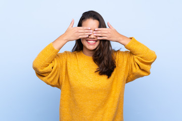 Young Colombian girl with sweater over isolated blue background covering eyes by hands