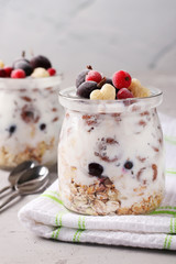 Granola crispy honey muesli with frozen black and red currant and natural yogurt, a delicious and healthy breakfast, located in glass jars on a gray background