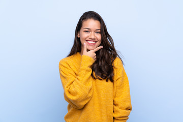 Young Colombian girl with sweater over isolated blue background smiling