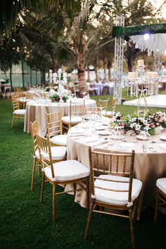 International Wedding outdoor celebration party under palm trees. Served tables on green area in hotel. Landyard. Beige and pink colors. Close-up and wide angle.