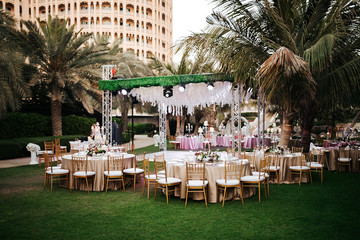 International Wedding outdoor celebration party under palm trees. Served tables on green area in hotel. Landyard. Beige and pink colors. Close-up and wide angle. - 341813208