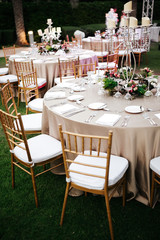 International Wedding outdoor celebration EVENING party under palm trees. Served tables on green area in hotel. Landyard. Beige and pink colors. Close-up and wide angle.