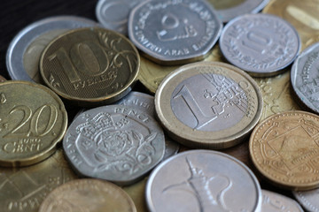 A collection of coins of different countries lies on a wooden table next to each other. Focus on one euro coin of European Union. Theme of the world economy.