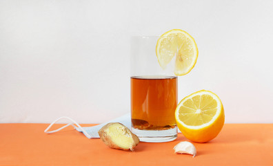 Medical mask, a glass of tea with lemon and ginger. The face mask protects against environmental pollution, flu viruses and coronavirus. Maintenance of immunity.