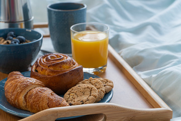 Breakfast served in bed on wooden tray with coffee and croissants