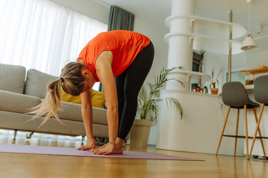 Photo of young woman practicing yoga bending forward on yoga mat. Young woman is stretching after workout at home in self quarantine.
