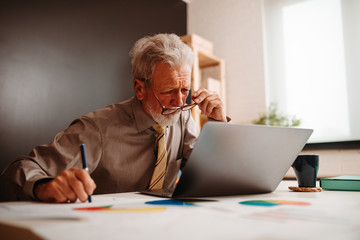 Close shot of elderly businessman with glasses looking at laptop in office.