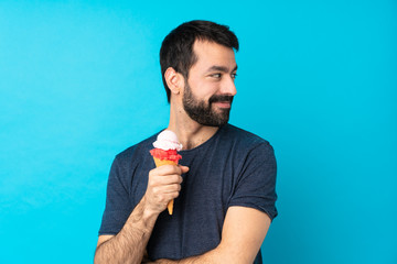 Young man with a cornet ice cream over isolated blue background with arms crossed and happy